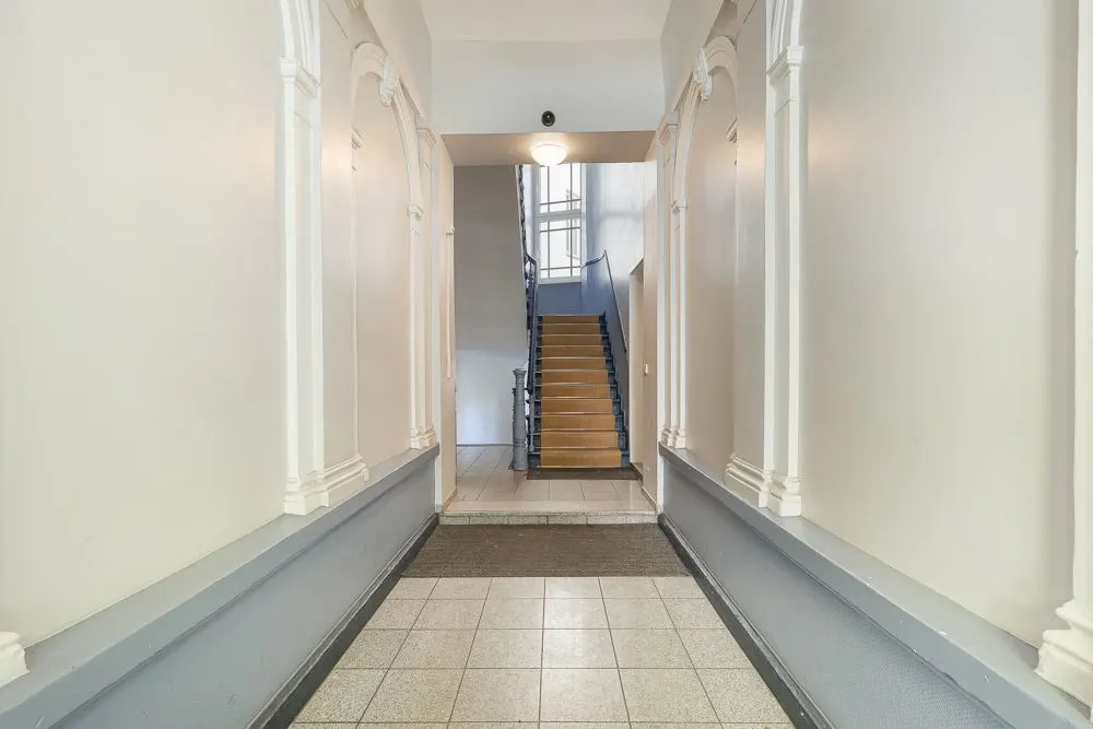 Heller Flur mit Fliesenboden und einer Treppe am Ende, Wände mit Zierleisten.