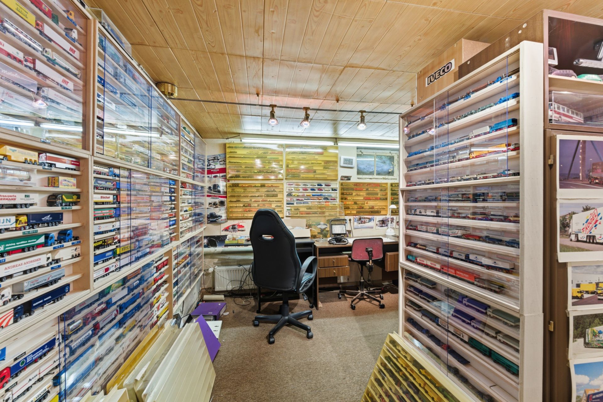 Zimmer mit Regalen voller Modellfahrzeuge, zwei Schreibtischen und Bürostühlen.