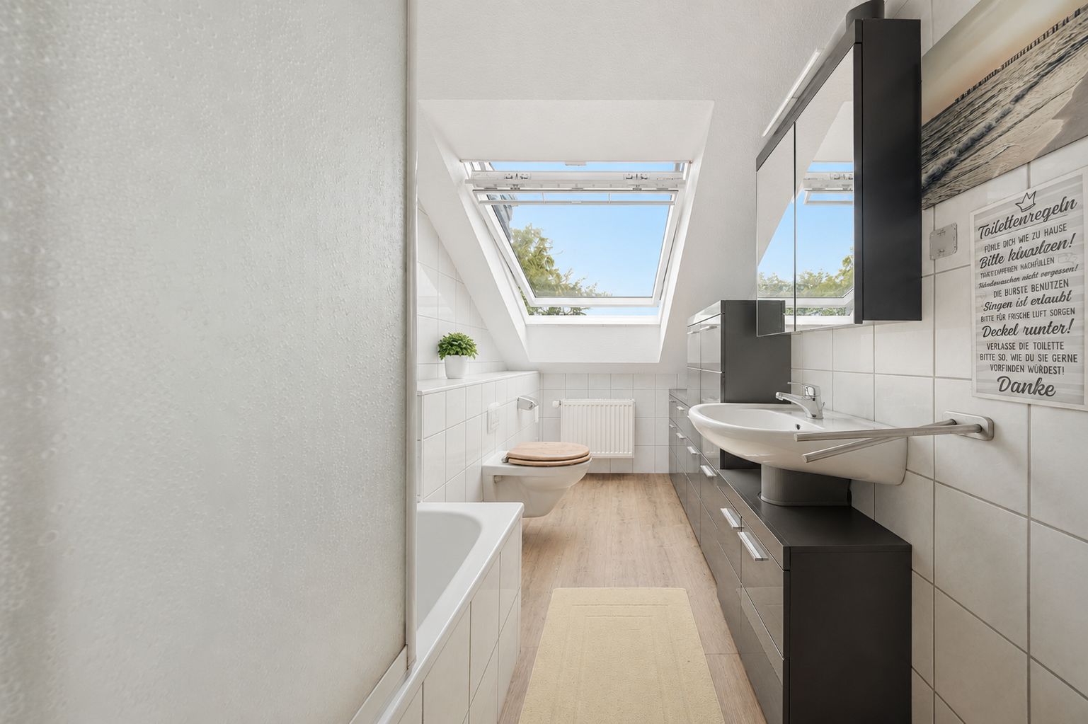 Helles Badezimmer mit Dachfenster, Badewanne, Waschbecken, Spiegel und WC.