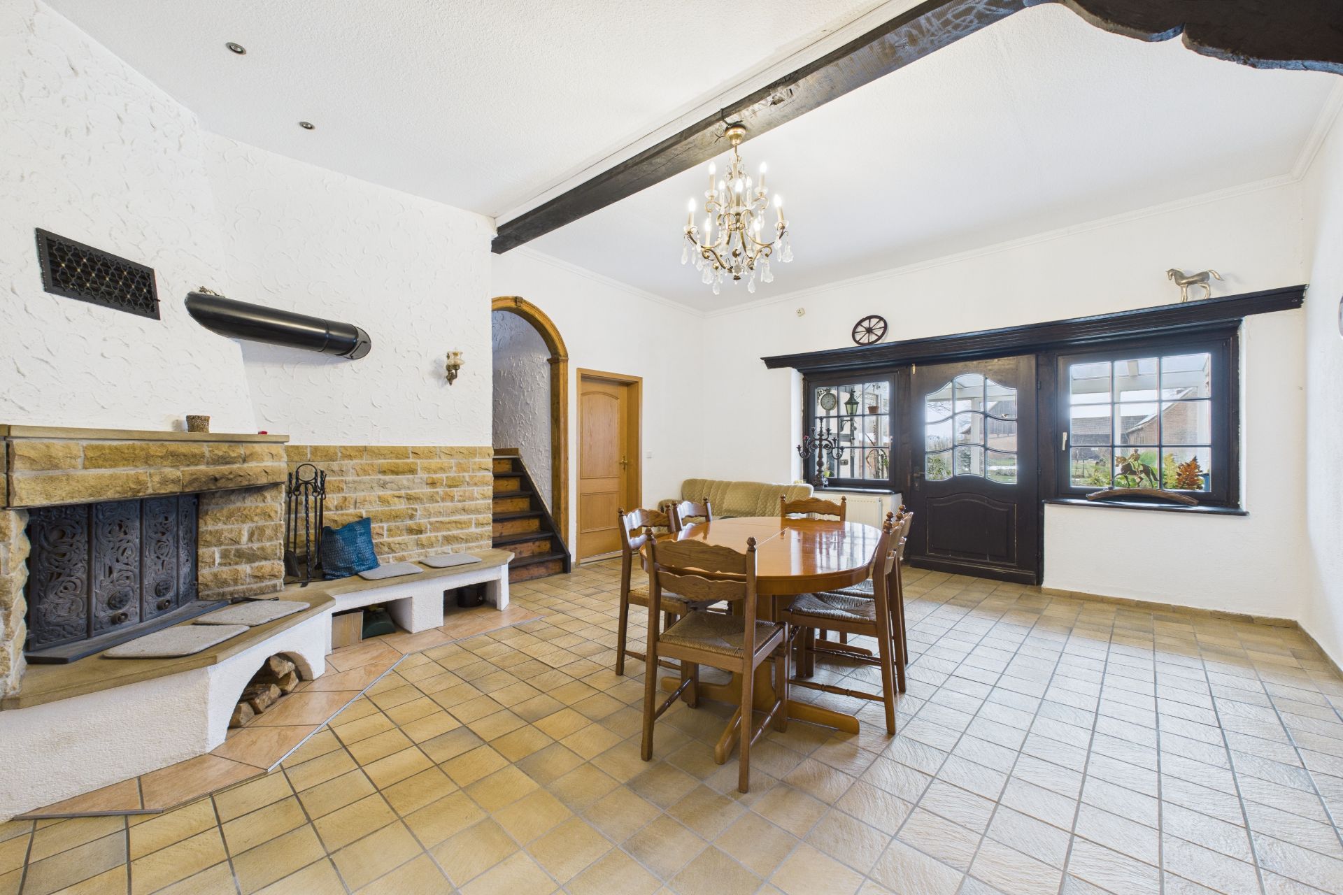Helles Wohnzimmer mit Kamin, Holztisch, Stühlen, Sofa und großen Fenstern.