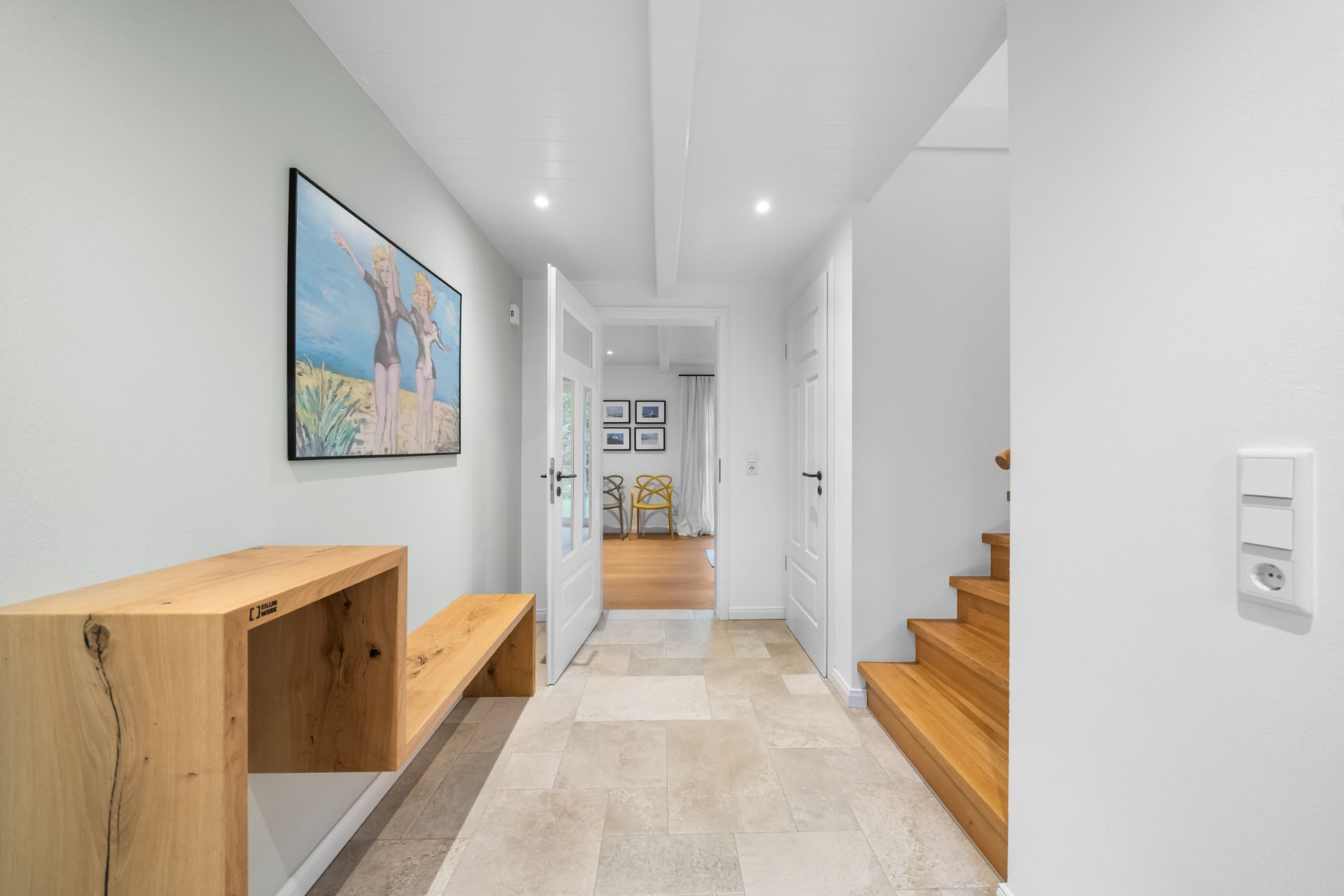Heller Flur mit Holzbank, Wandbild, weißen Türen und Holztreppe in einem Wohnhaus.