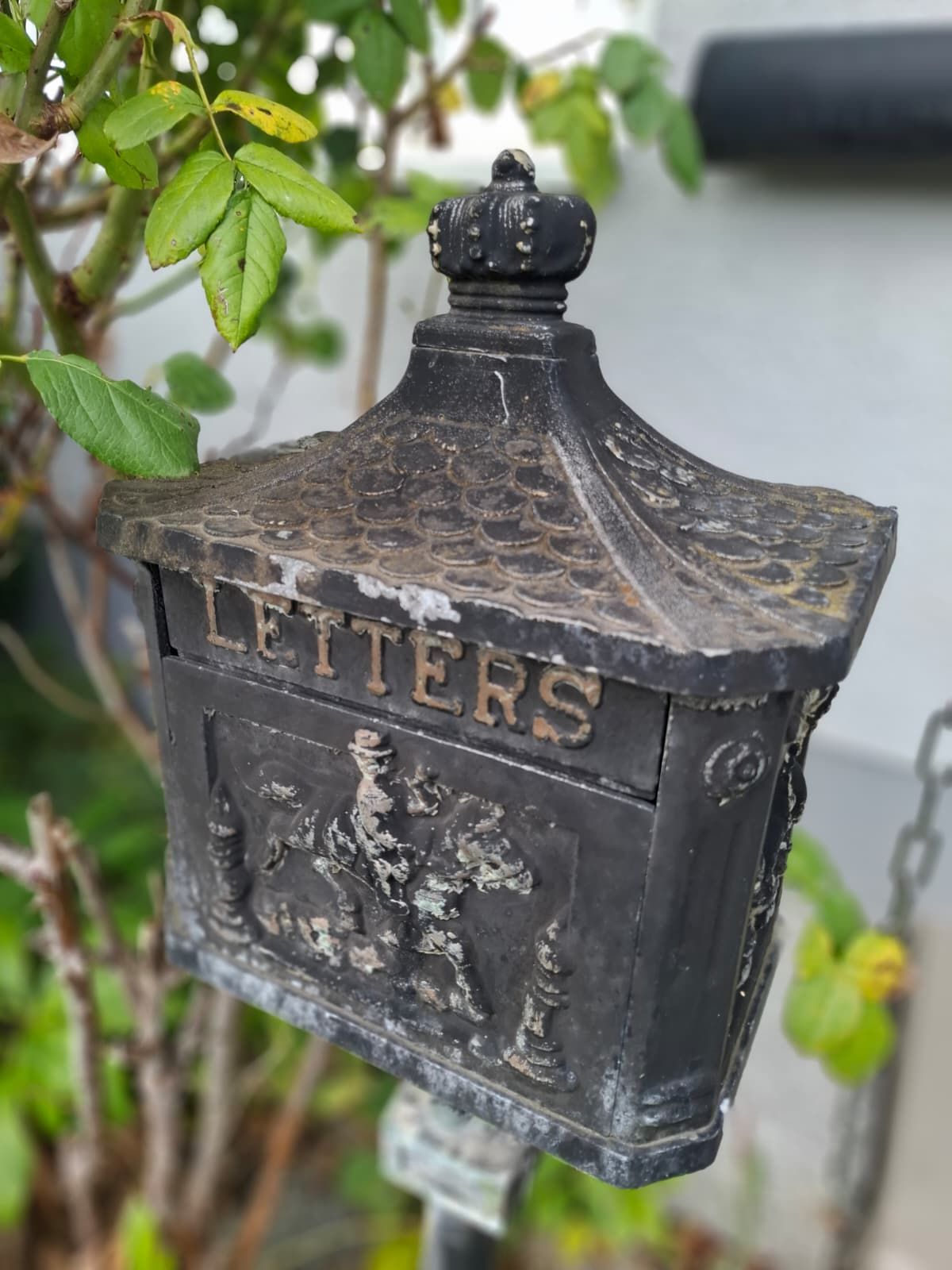 Alter, schwarzer Briefkasten mit Ornamenten und der Aufschrift 'LETTERS' im Vorgarten.