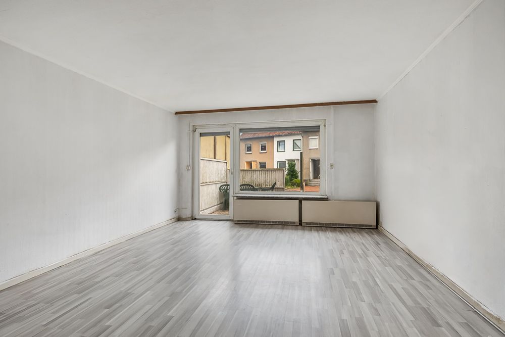 Leeres Wohnzimmer mit großem Fenster und Tür zur Terrasse, Blick auf Nachbarhäuser.