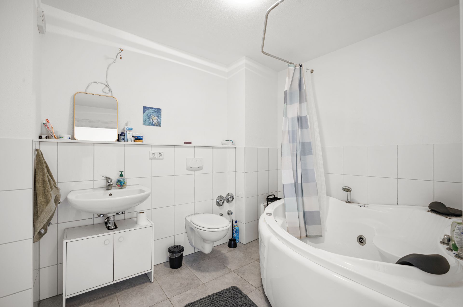 Modernes Badezimmer mit Eckbadewanne, Waschbecken, Spiegel und WC, helle Fliesen und Duschvorhang.