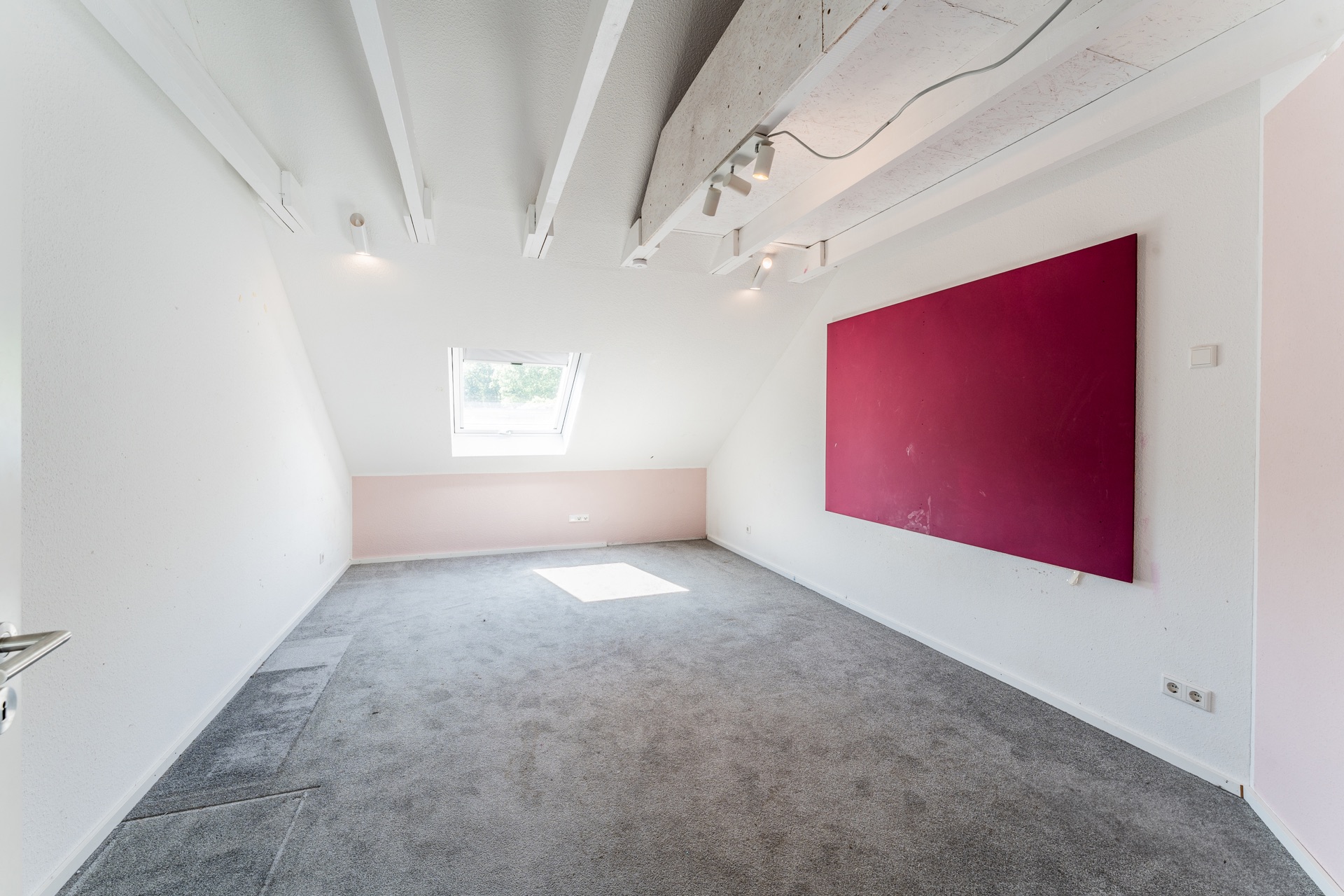 Heller Raum mit grauem Teppich, Schrägdecke, Dachfenster und großem roten Wandbild.