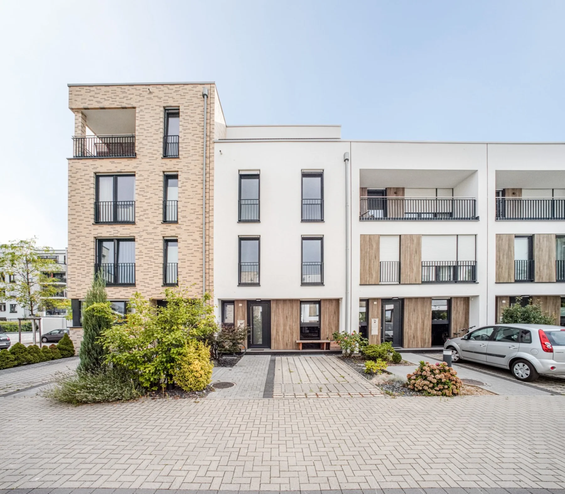 Moderne Wohnhausfassade mit drei Stockwerken, Balkonen und parkenden Autos davor.