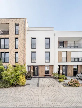 Moderne Wohnhausfassade mit drei Stockwerken, Balkonen und parkenden Autos davor.