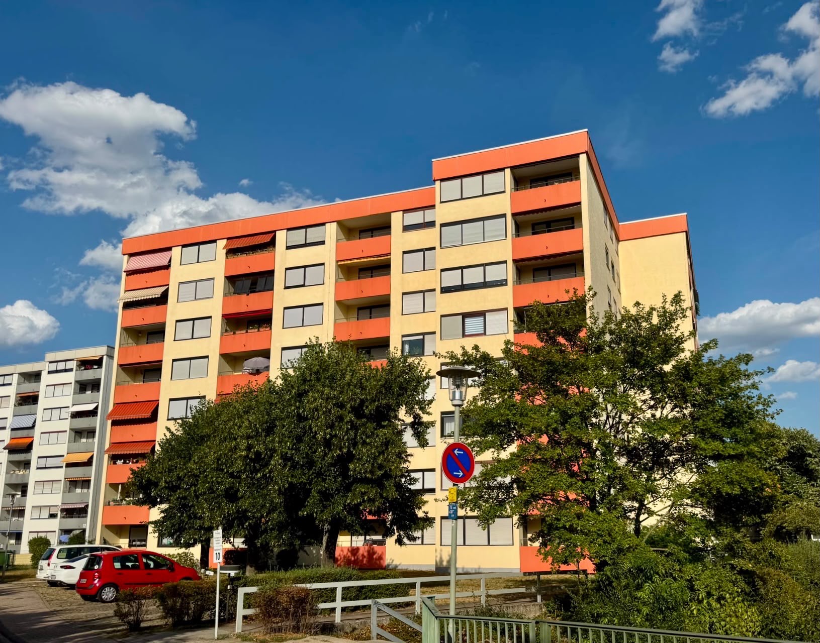 Mehrstöckiges Wohnhaus mit orange-gelben Fassaden und Bäumen im Vordergrund.