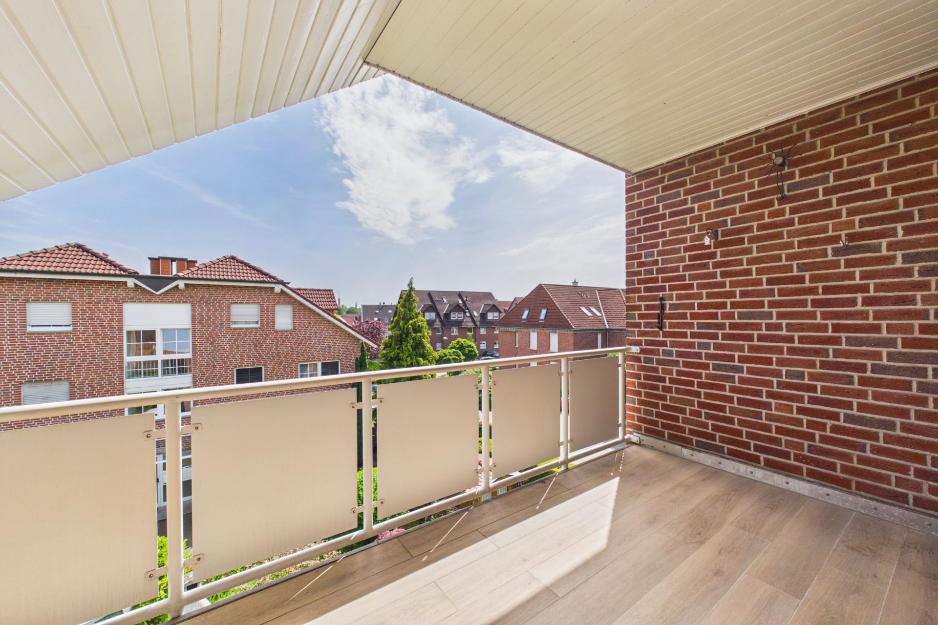 Überdachter Balkon mit Holzboden und Blick auf Nachbarhäuser aus rotem Backstein.