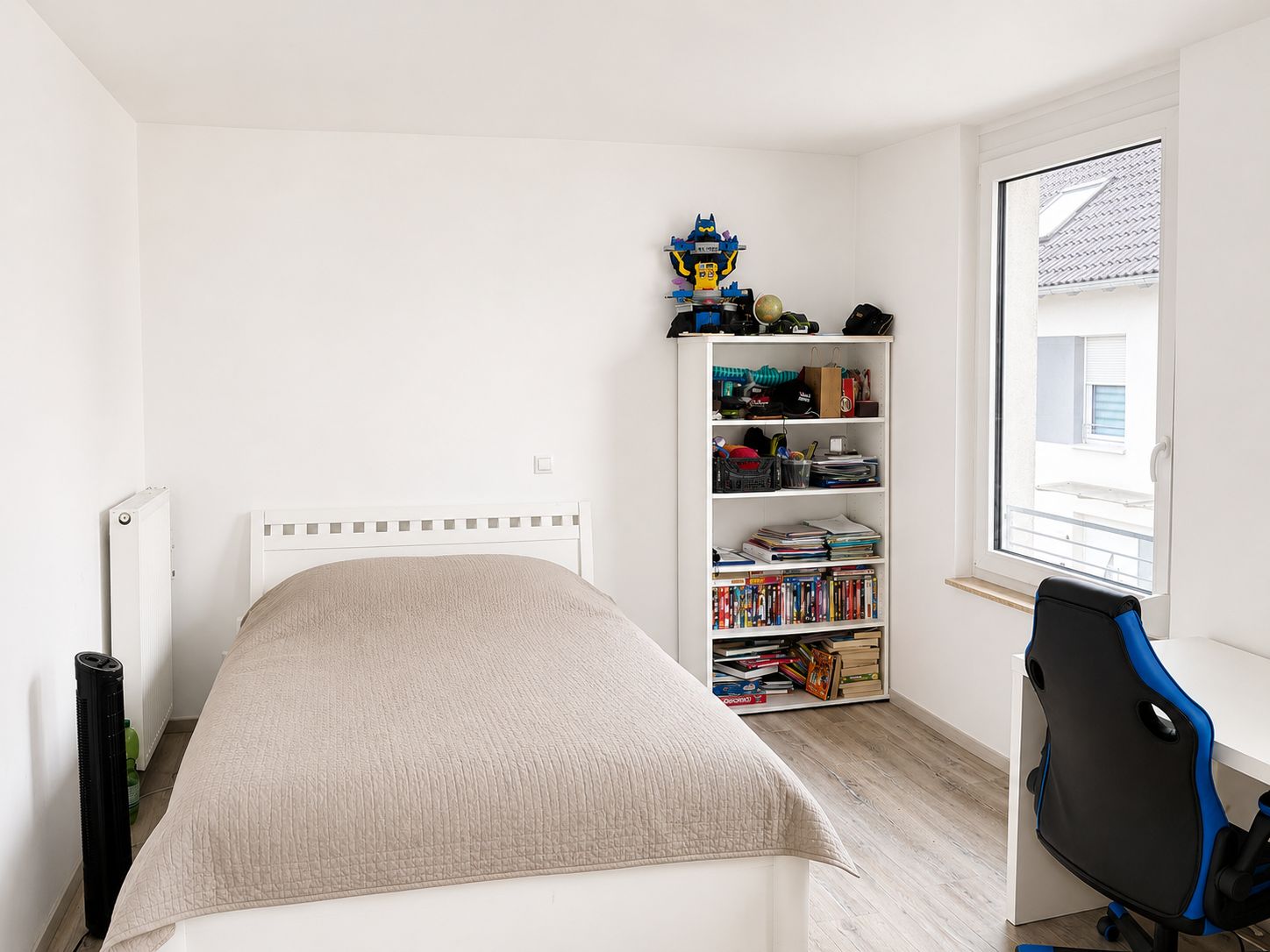 Helles Schlafzimmer mit Einzelbett, Bücherregal, Schreibtisch und Fenster.