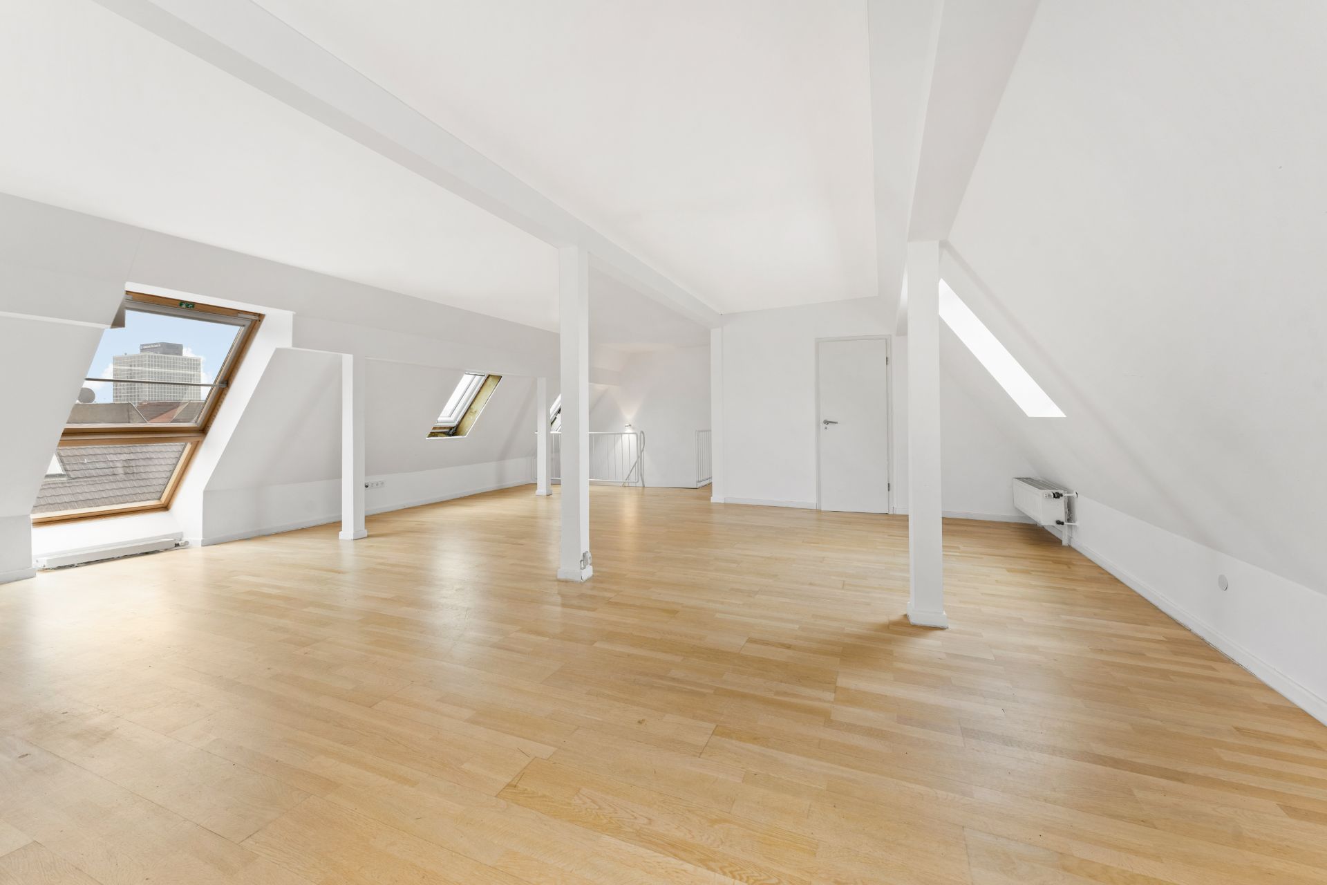 Helles Dachgeschosszimmer mit schrägen Wänden, großen Fenstern und Parkettboden.
