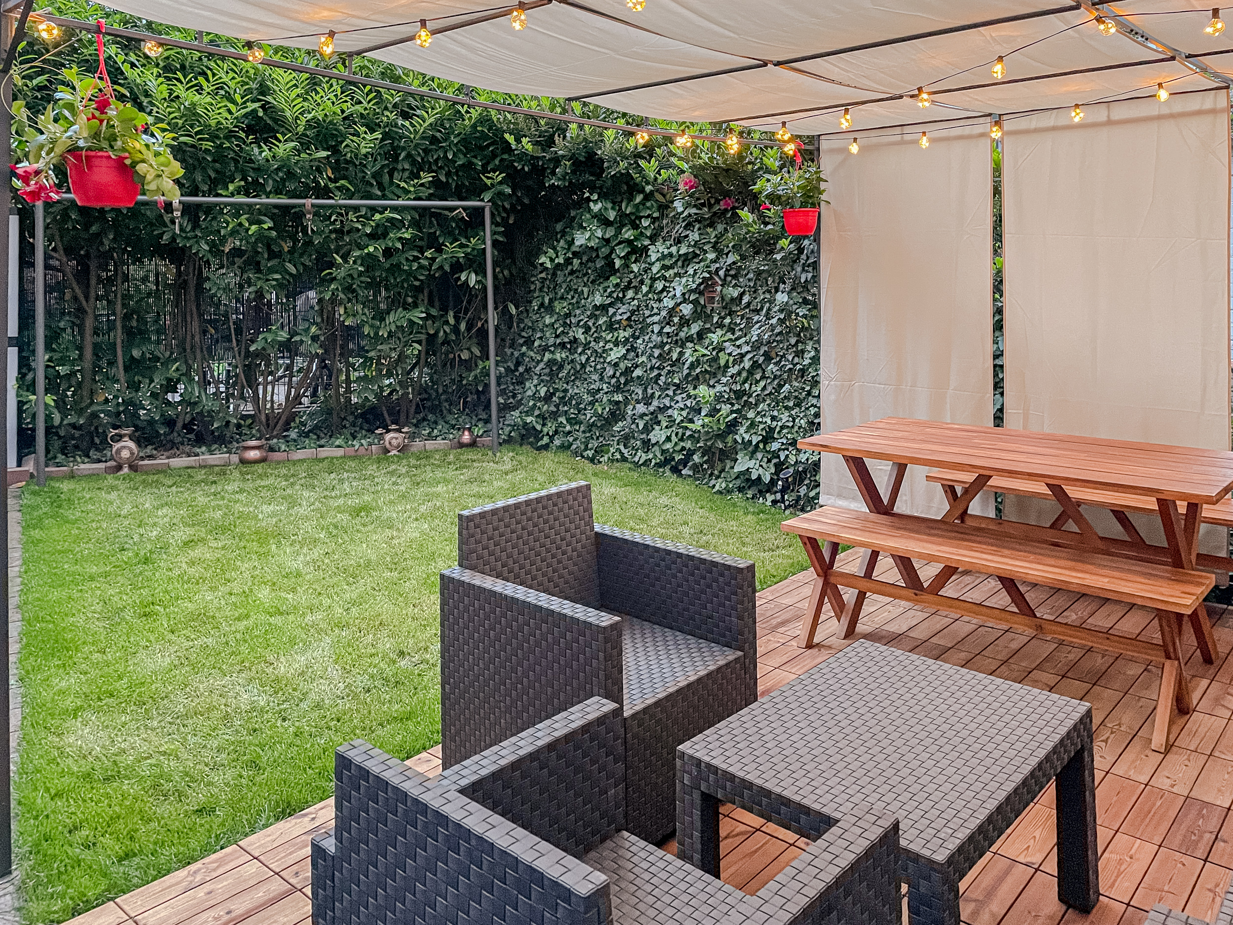 Überdachte Terrasse mit Sitzgruppe, Holztisch, Bänken, Lichterkette und angrenzendem Garten.