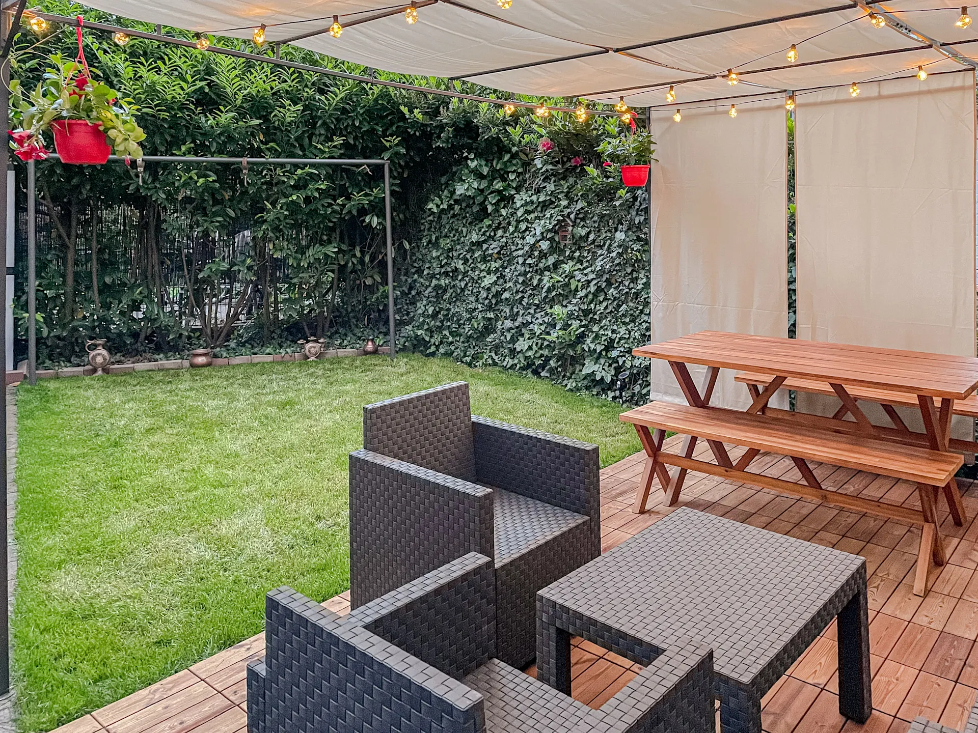 Überdachte Terrasse mit Sitzgruppe, Holztisch, Bänken, Lichterkette und angrenzendem Garten.