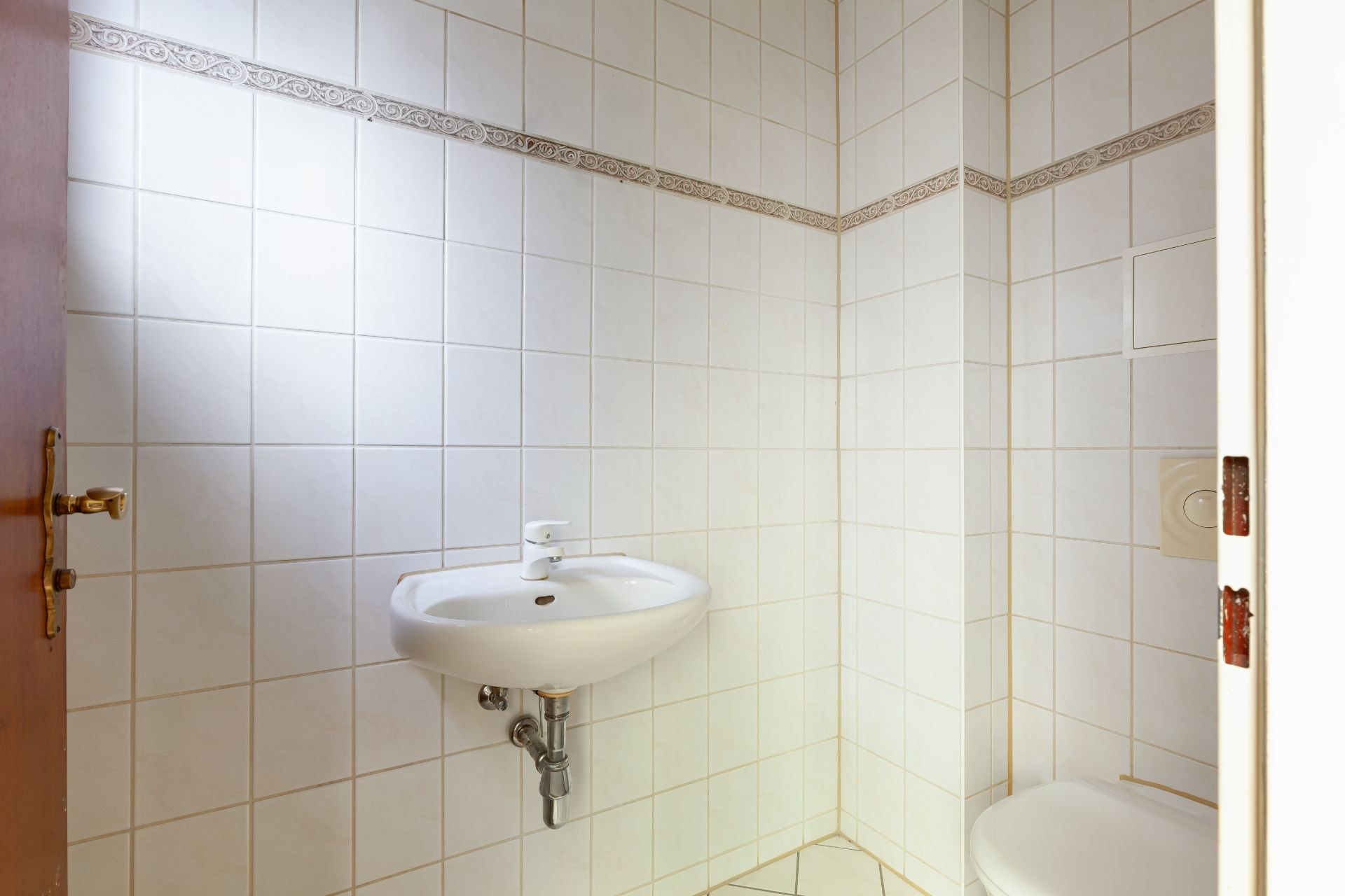 Kleines, gefliestes Badezimmer mit Waschbecken und Toilette.