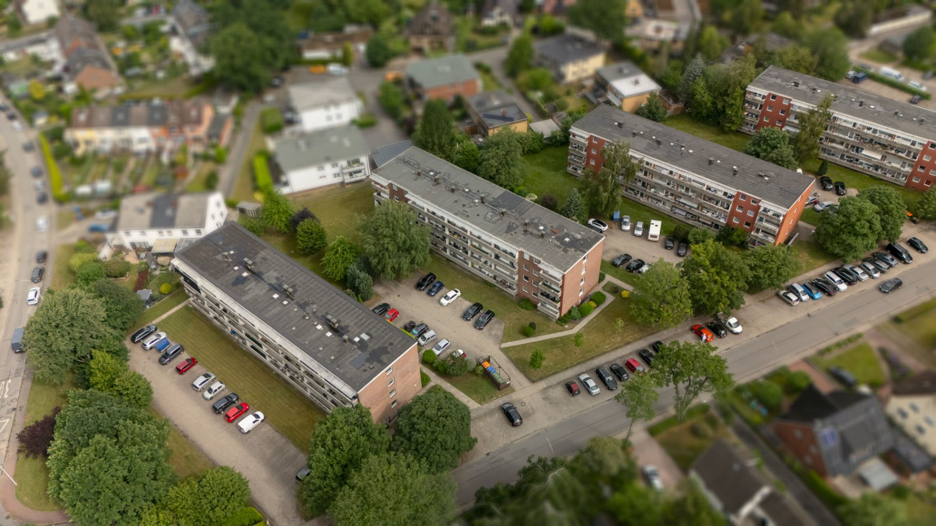 Luftaufnahme von mehreren Wohngebäuden mit Parkplätzen und Bäumen in einer Siedlung.