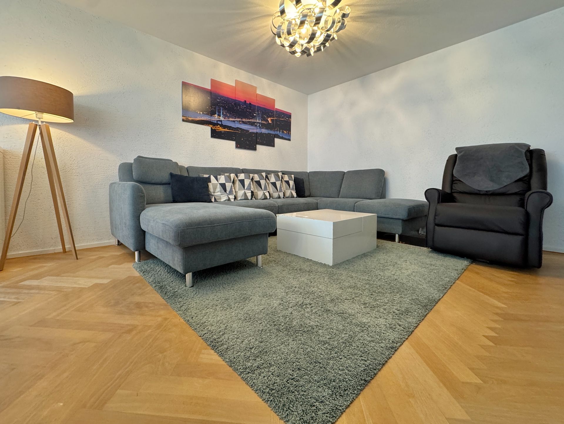 Modernes Wohnzimmer mit grauem Ecksofa, Sessel, Teppich und Stehlampe.