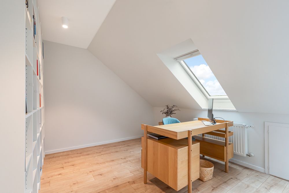 Helles Arbeitszimmer mit Dachfenster, Holzboden, Schreibtisch und Regal an der Wand.