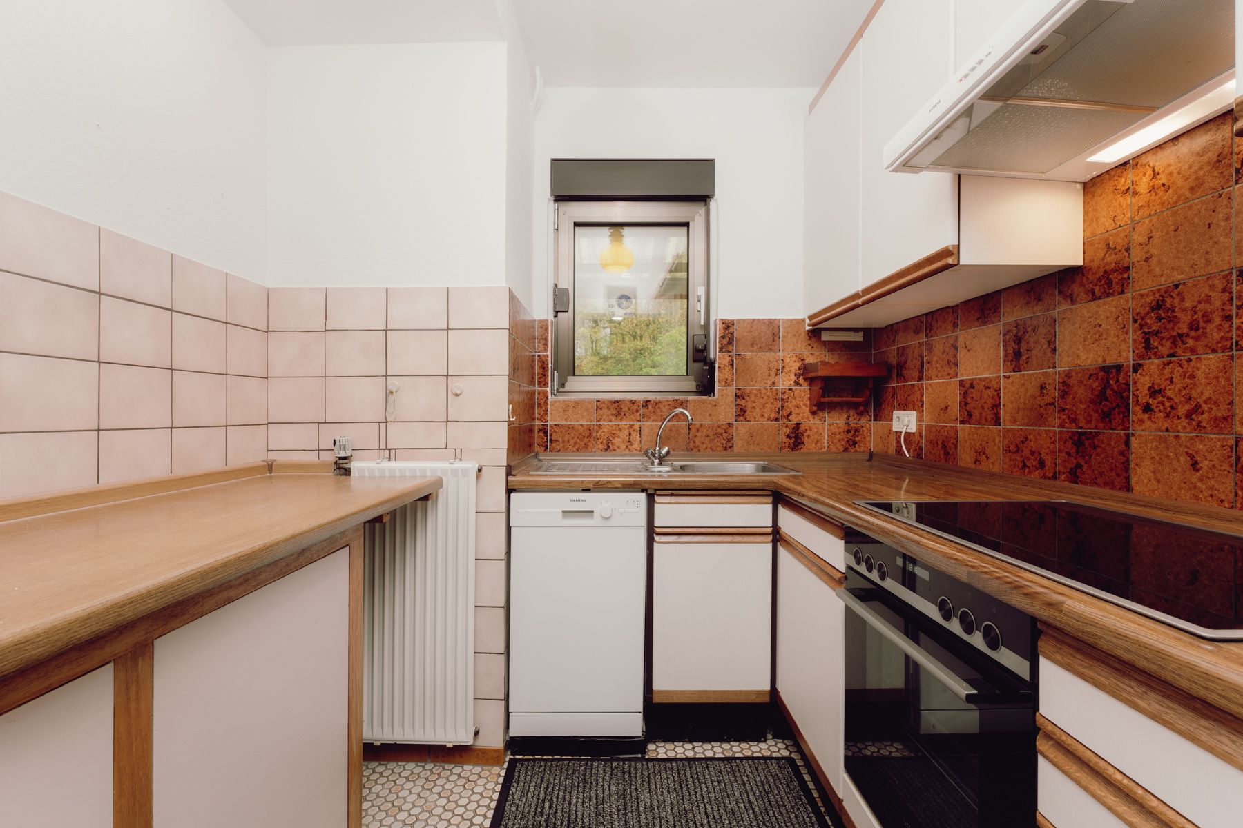 Kleine Küche mit Holzarbeitsplatte, Herd, Spülmaschine und Fenster über der Spüle.