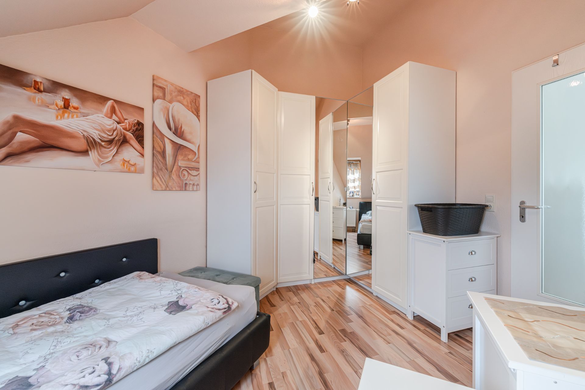 Schlafzimmer mit Einzelbett, weißen Schränken, Kommode und Spiegel, Holzfußboden.