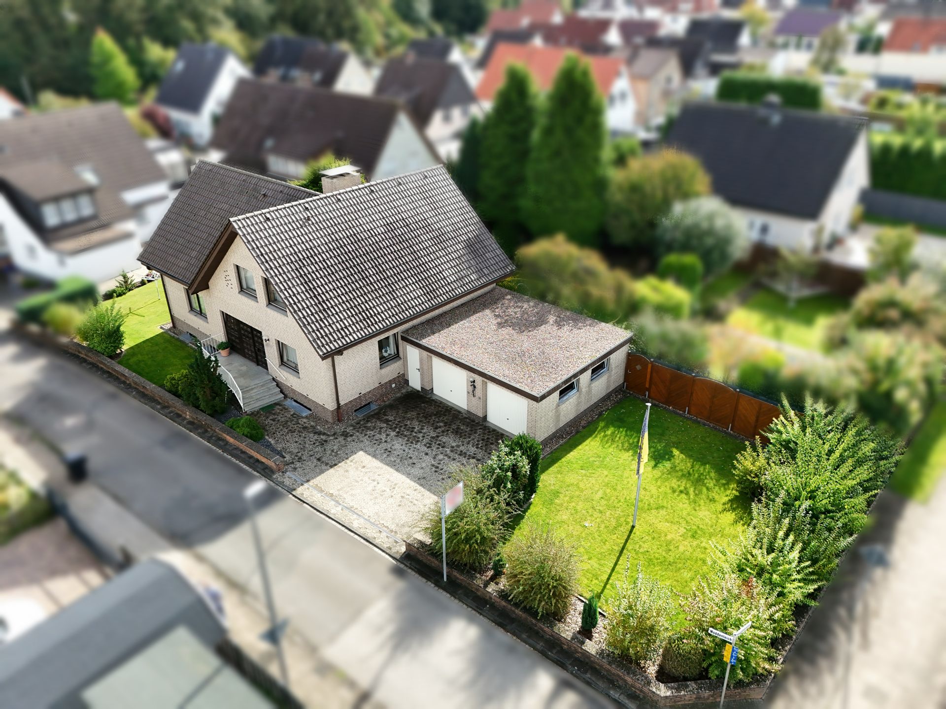 Luftaufnahme eines Einfamilienhauses mit Garage und kleinem Garten an einer Wohnstraße.