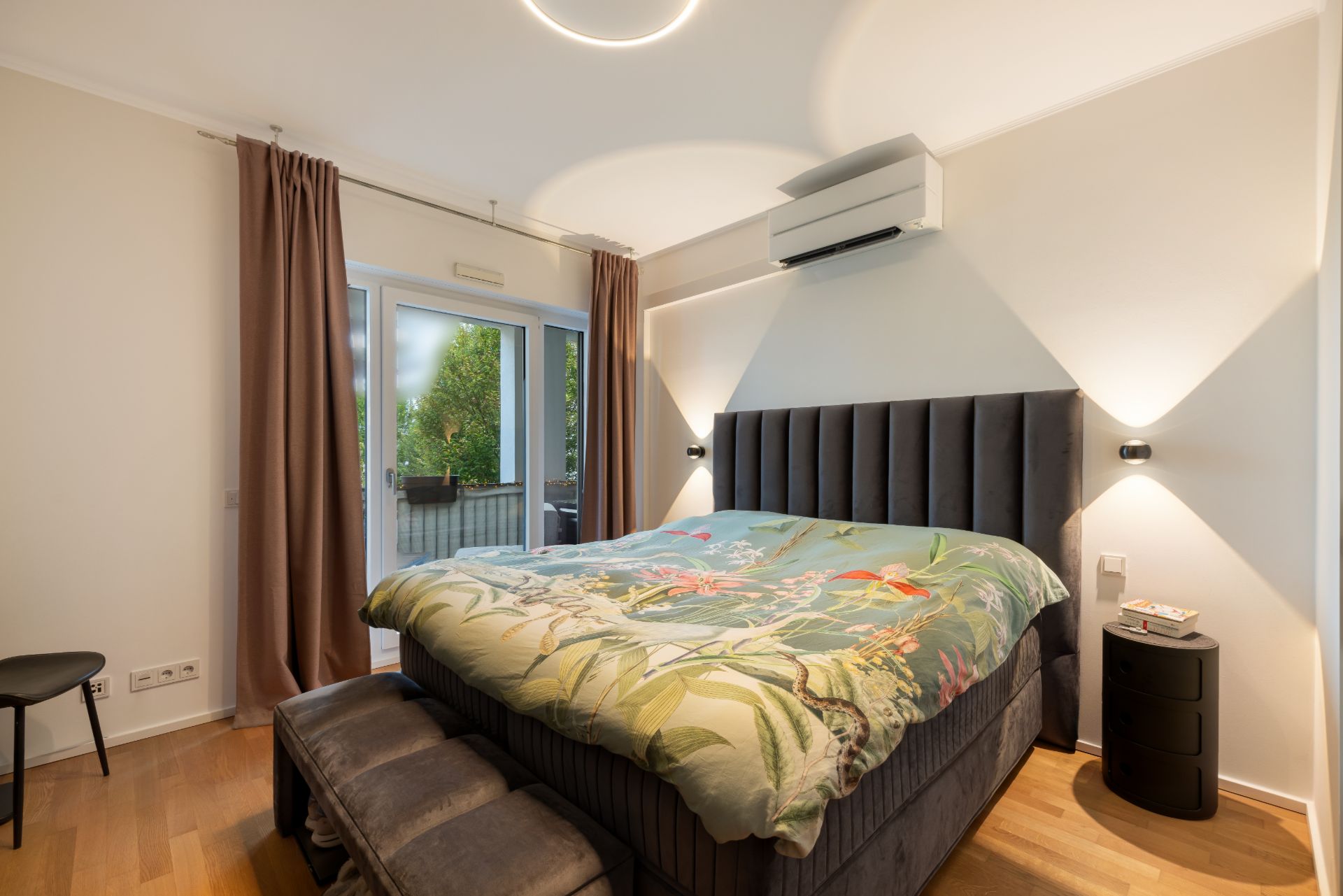 Modernes Schlafzimmer mit großem Bett, Nachttisch, Stuhl, Holzboden und Blick auf Terrasse.
