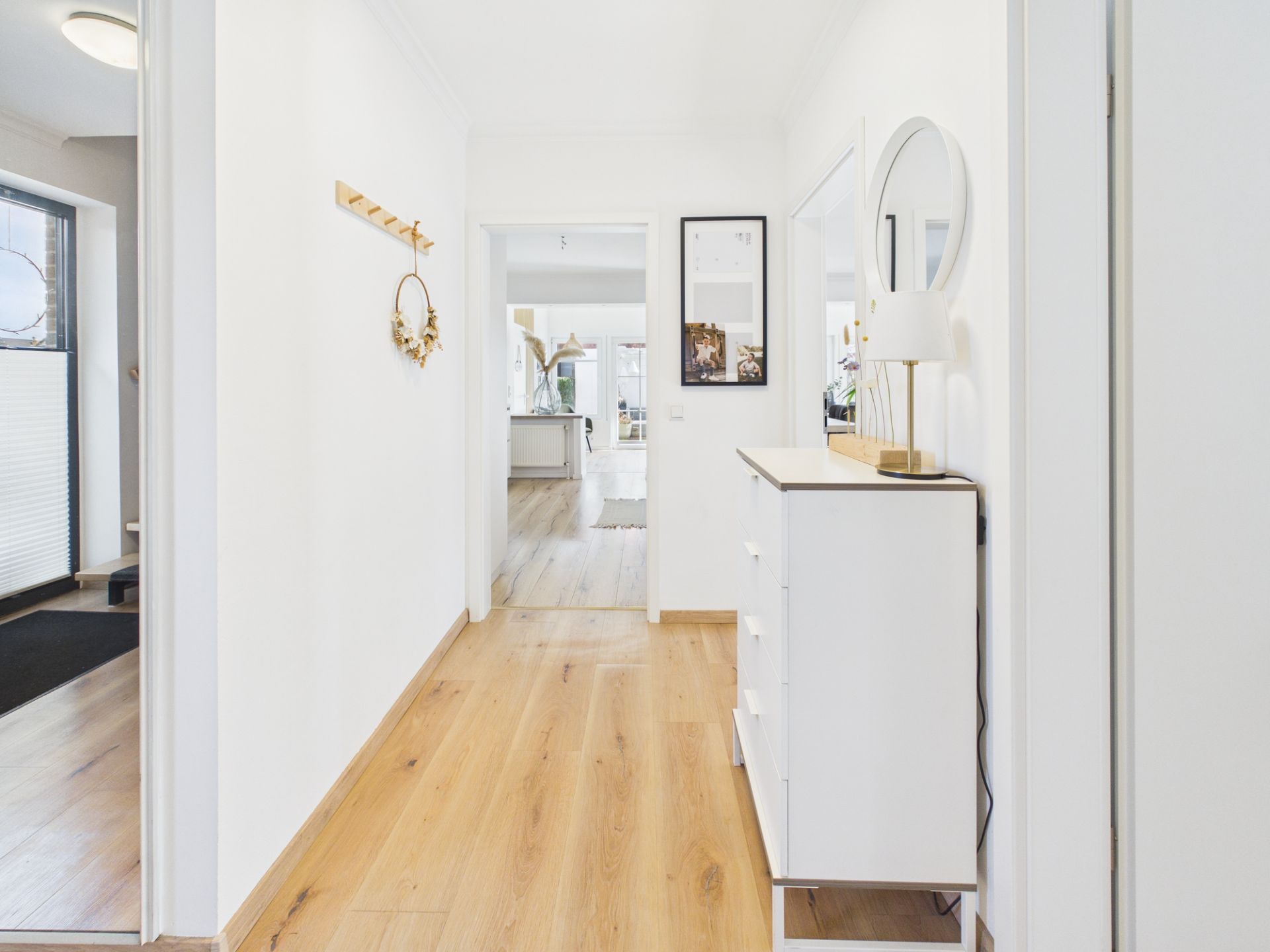 Heller Flur mit Holzfußboden, Kommode, rundem Spiegel und Garderobe an der Wand.