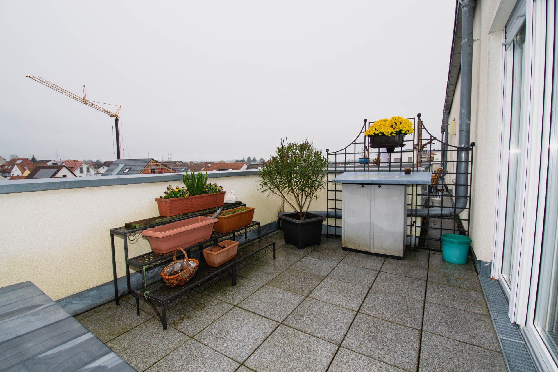 Balkon mit Pflanzgefäßen, kleinem Tisch und Ausblick auf Stadt und Baukran.