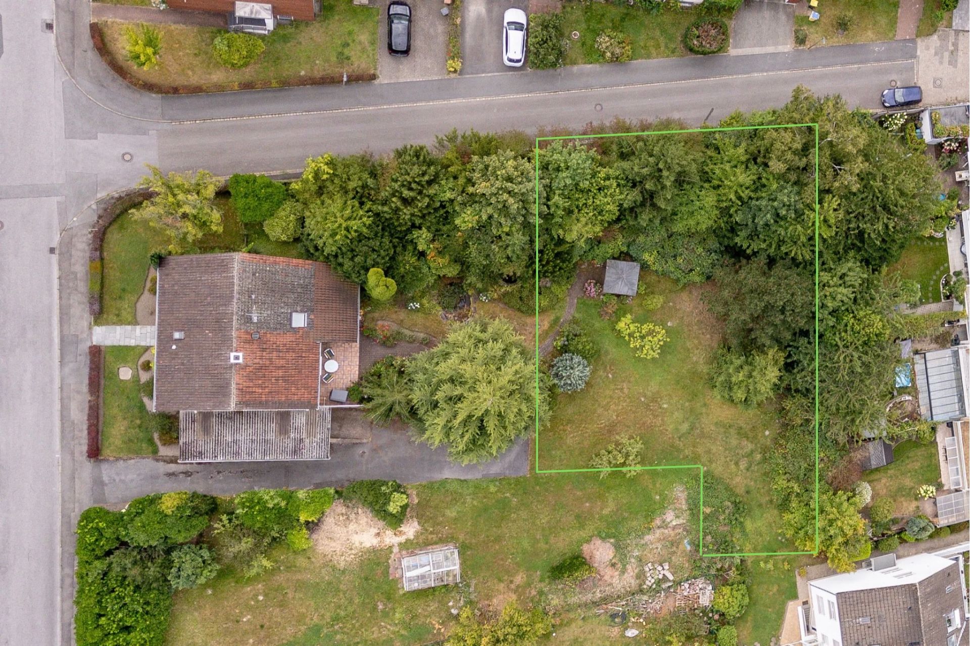 Luftaufnahme eines Hauses mit Garten, umgeben von Bäumen und Straßen, grüner Bereich markiert.