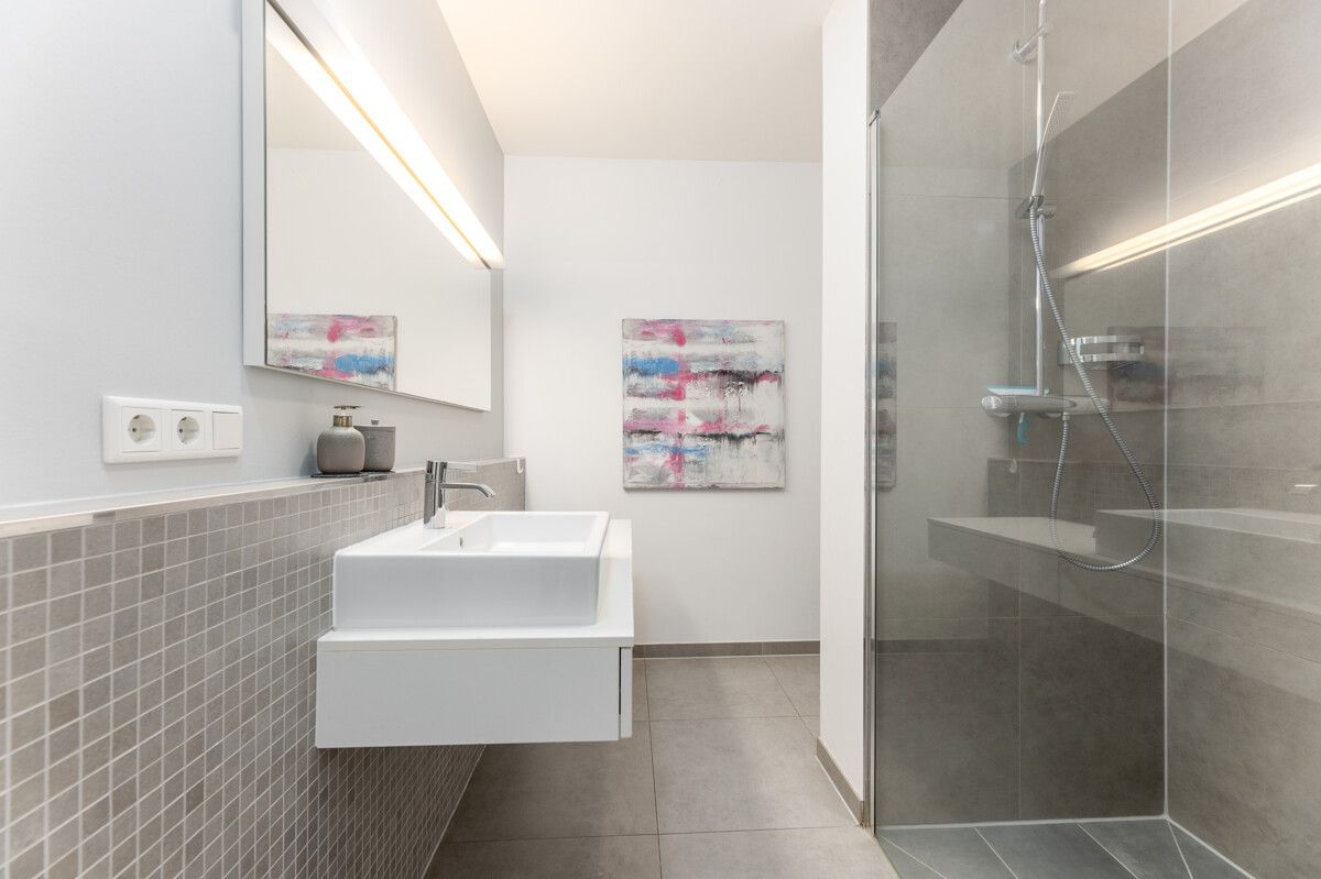 Modernes Badezimmer mit Waschbecken, großem Spiegel und begehbarer Dusche.