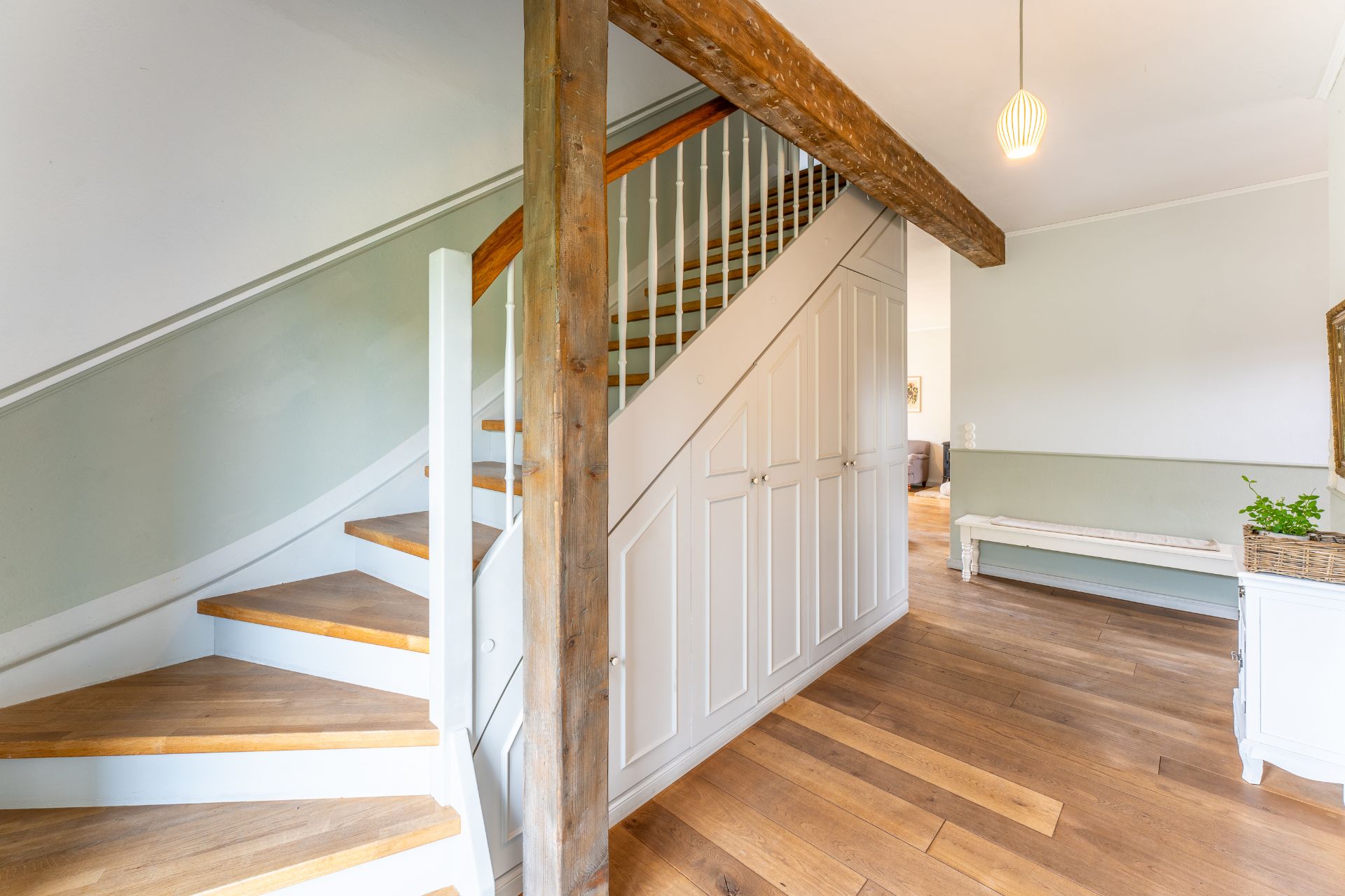 Heller Flur mit Holztreppe, Einbauschränken und Sitzbank auf Holzfußboden.