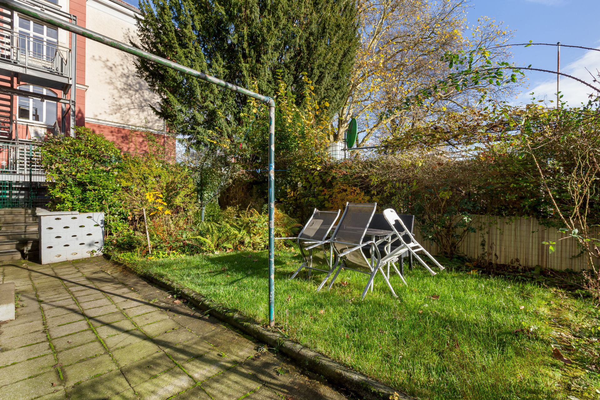 Kleiner Garten mit Rasenfläche, Gartenmöbeln und angrenzender Terrasse, umgeben von Büschen.