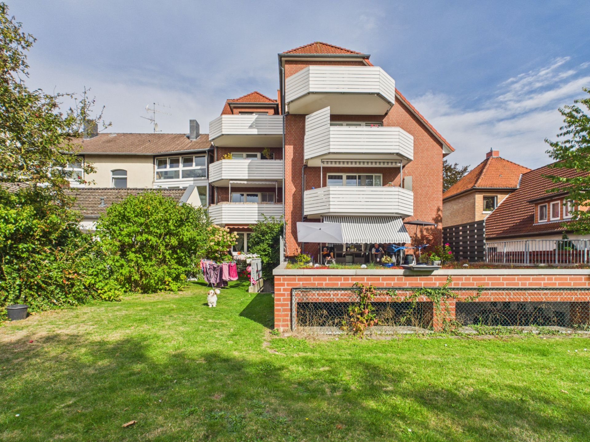 Mehrfamilienhaus mit Balkonen, Gartenfläche und Wäscheleinen im Vordergrund.