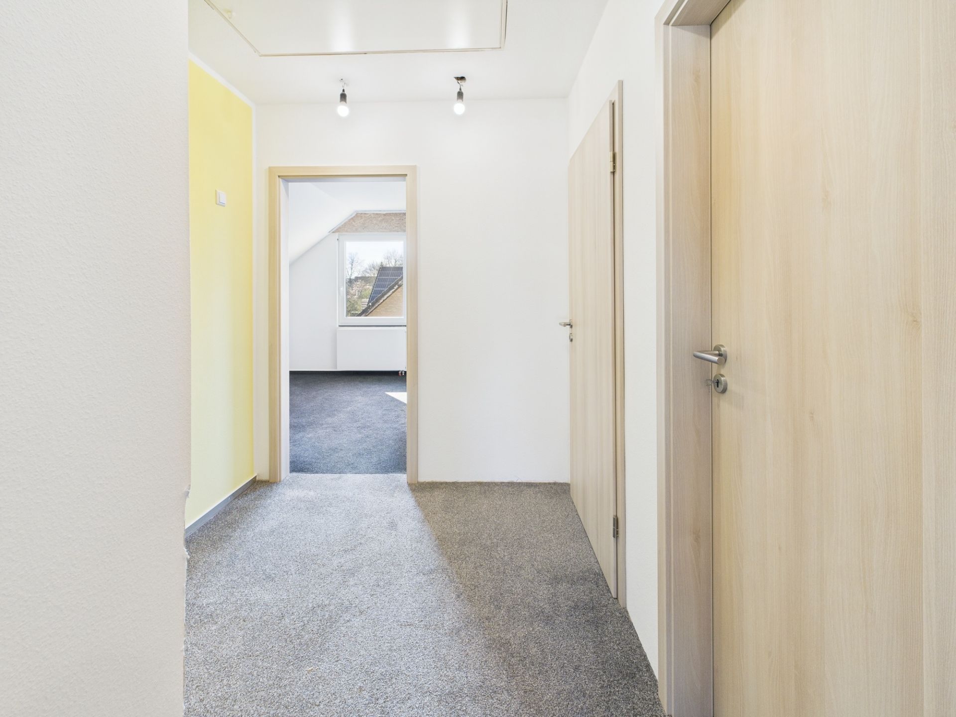 Heller Flur mit Teppichboden und drei Holztüren in einer Wohnung.