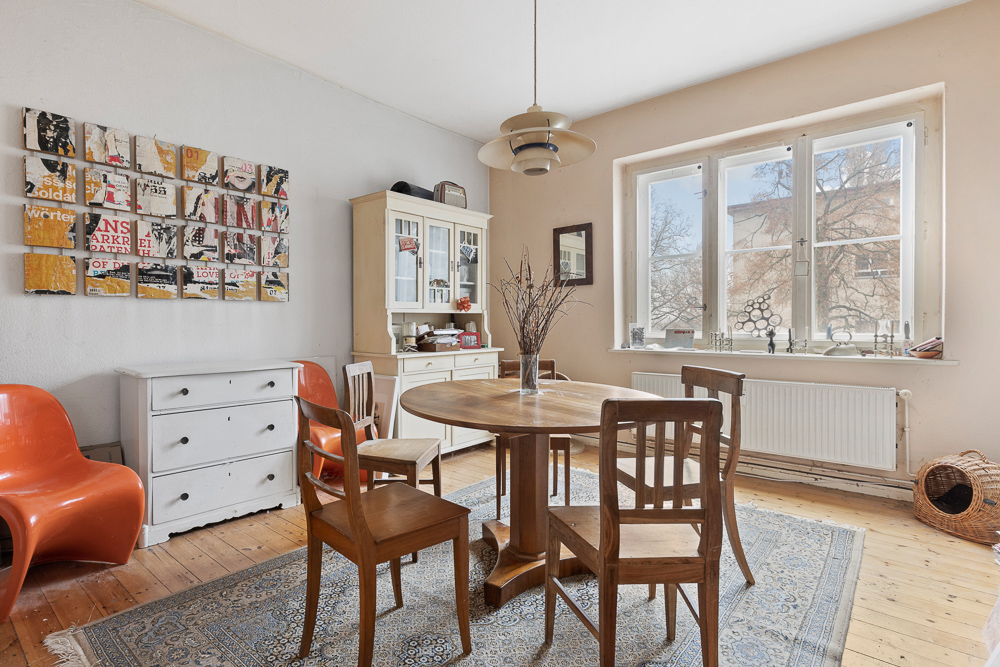 Heller Essbereich mit Holztisch, gemischten Stühlen und Sideboard vor großem Fenster.
