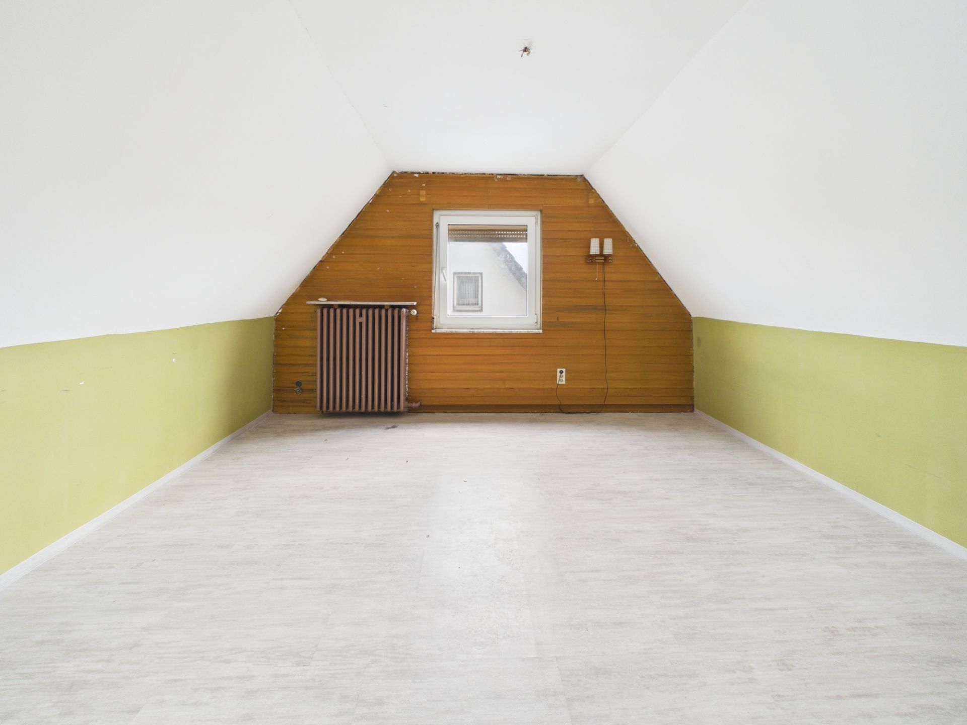 Leerer Dachbodenraum mit weißem Boden, grünen Wänden und Holzverkleidung an der Stirnwand.