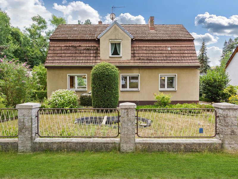 Einfamilienhaus mit rotem Dach, kleinem Garten und Zaun im Vordergrund.