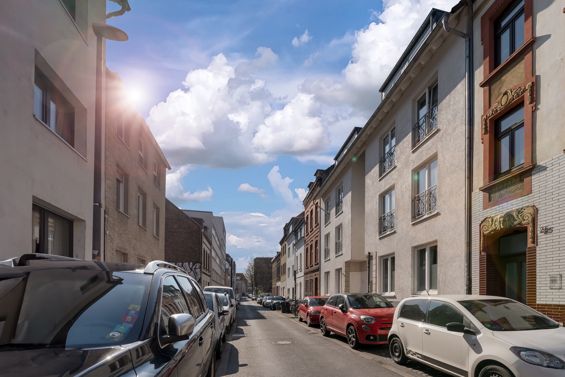 Wohnstraße mit parkenden Autos und mehrstöckigen Wohnhäusern bei Tageslicht.