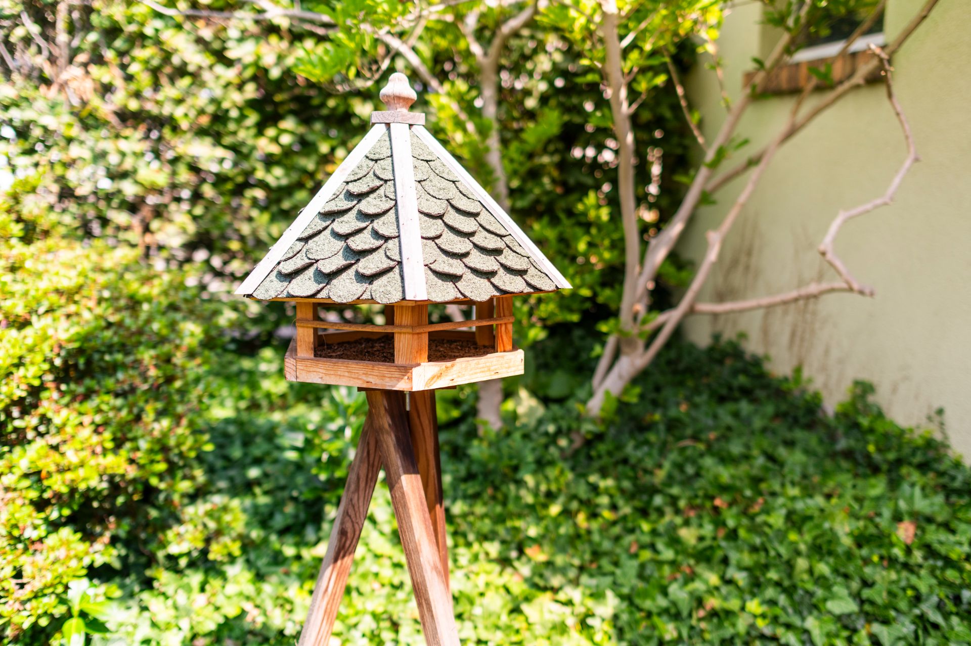 Ein hölzernes Vogelhaus mit Schindeldach steht im grünen Garten.