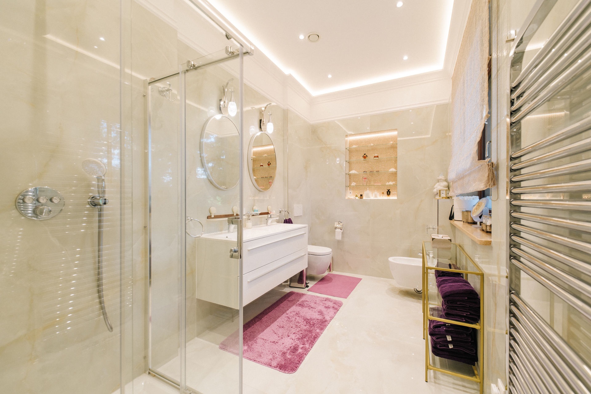 Modernes Badezimmer mit Dusche, Doppelwaschbecken, Spiegeln und lila Teppichen.