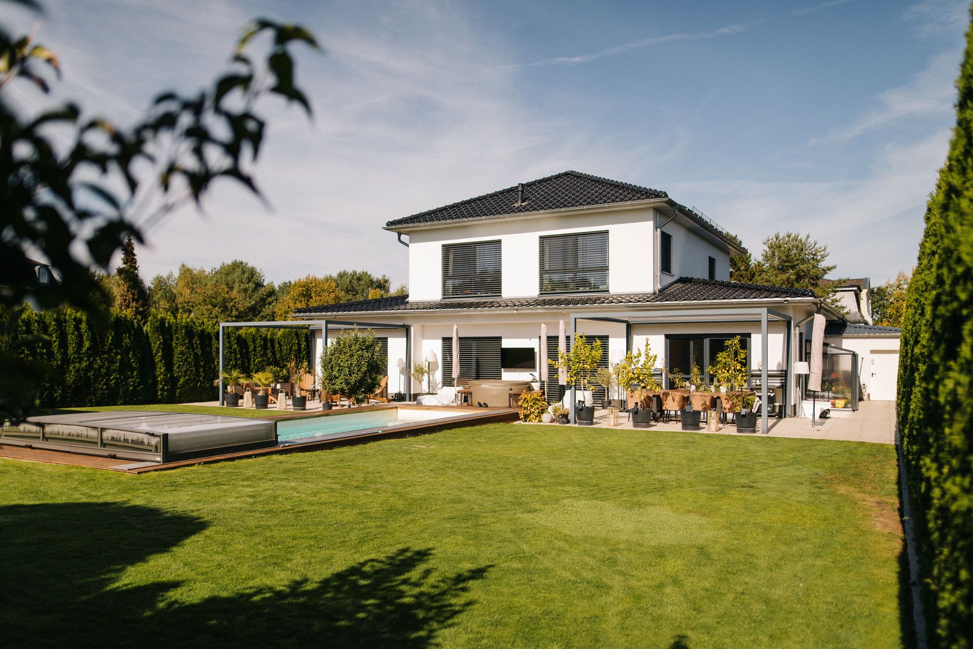 Modernes Einfamilienhaus mit Terrasse, Garten und Pool an einem sonnigen Tag.