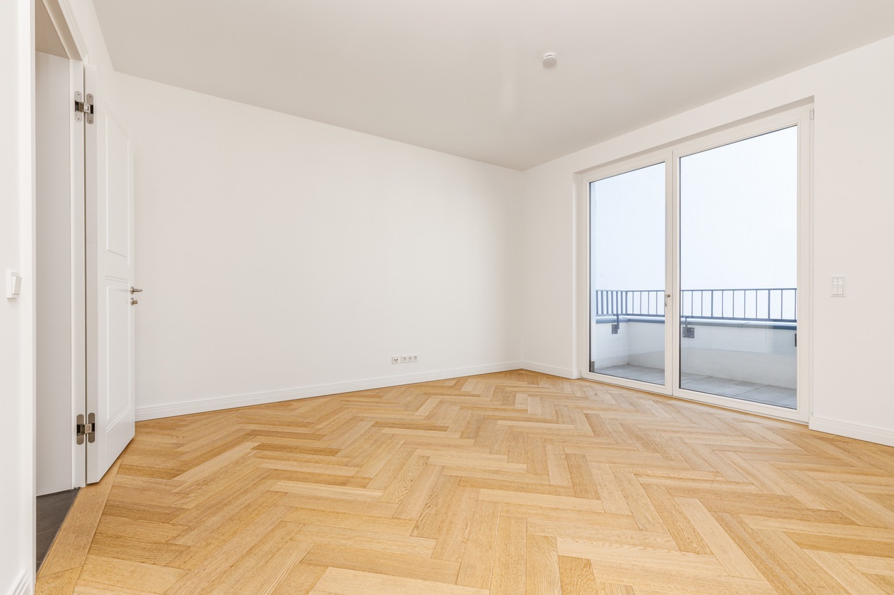 Leerer Raum mit Holzboden, weißen Wänden und großen Fenstertüren zu einem Balkon.