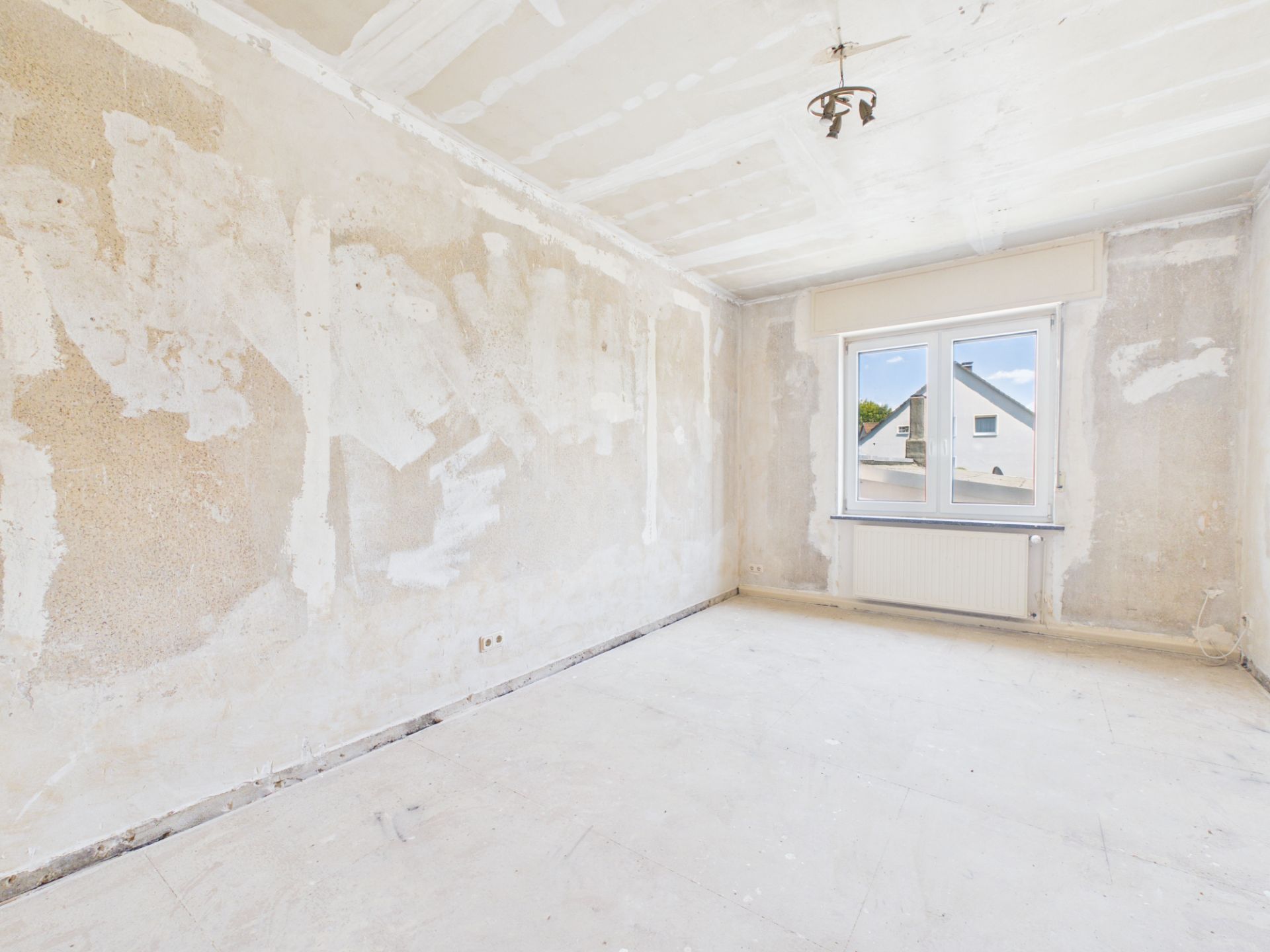 Leerer Raum mit unverputzten Wänden, Fenster und Deckenleuchte.