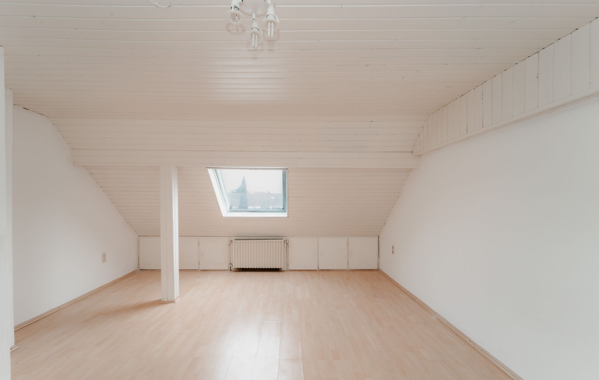 Heller Dachbodenraum mit Holzfußboden, weißer Decke, Dachfenster und Heizkörper.
