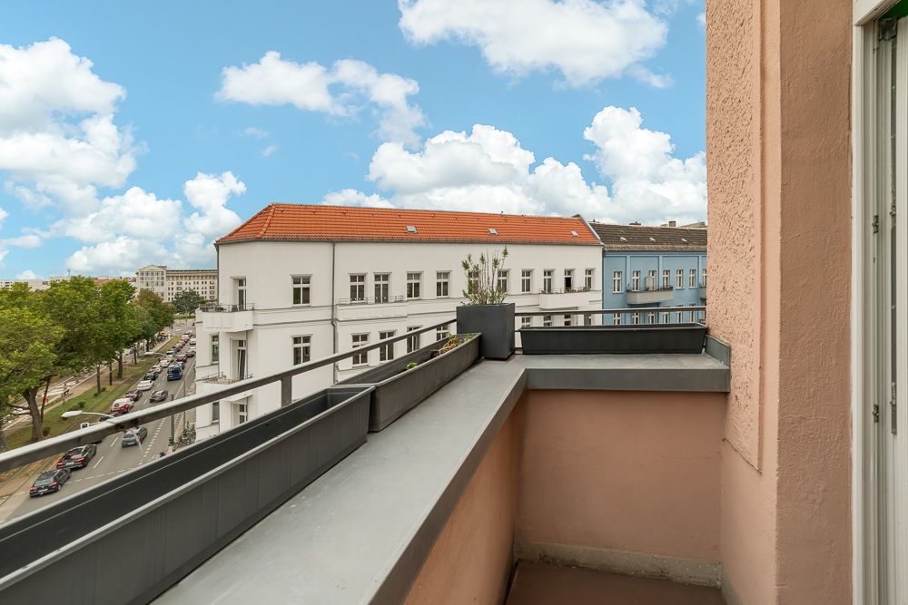 Kleiner Balkon mit Pflanzkübel, Blick auf Straße und Wohnhäuser bei blauem Himmel.