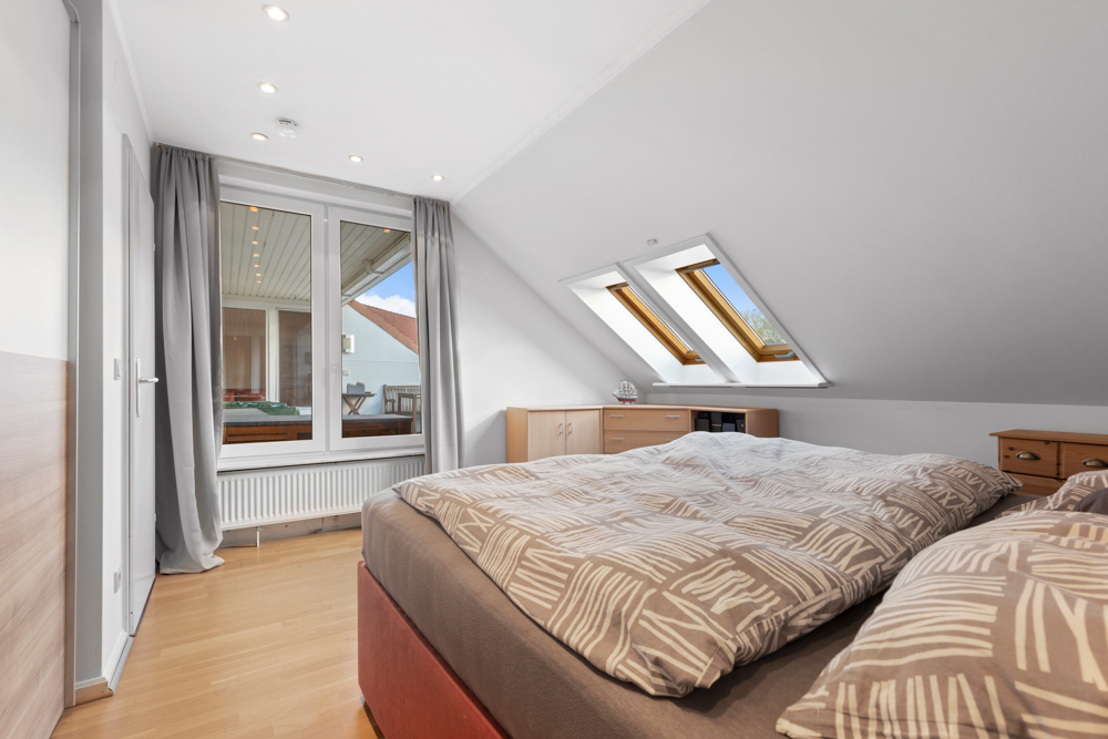 Helles Schlafzimmer mit Doppelbett, Dachfenstern und Zugang zu einem Balkon.