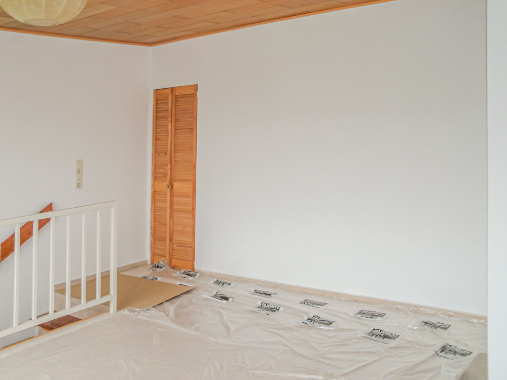 Leerer Raum mit Holzdecke, weißer Wand, Abdeckung auf dem Boden und kleiner Holztür.