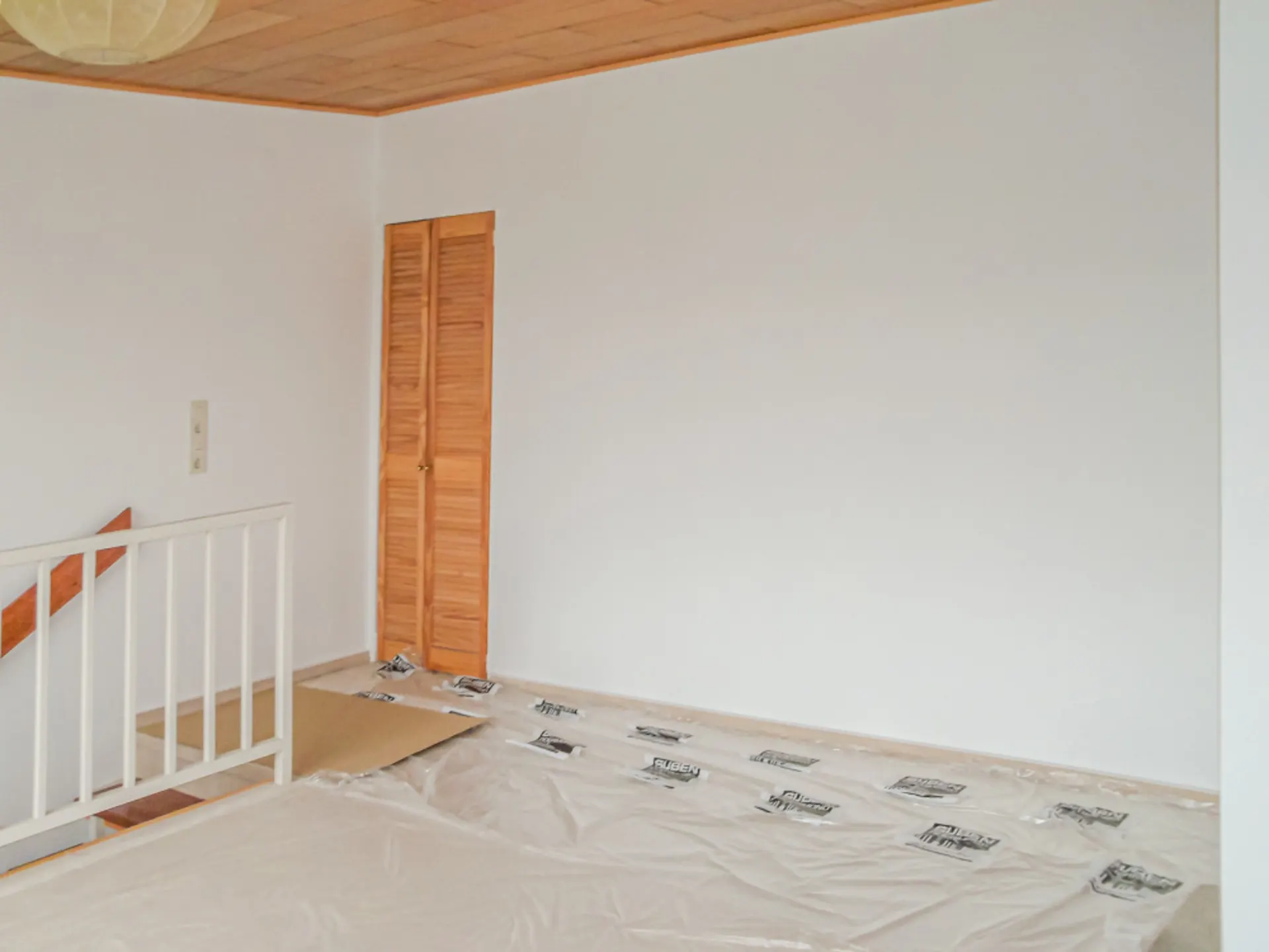 Leerer Raum mit Holzdecke, weißer Wand, Abdeckung auf dem Boden und kleiner Holztür.