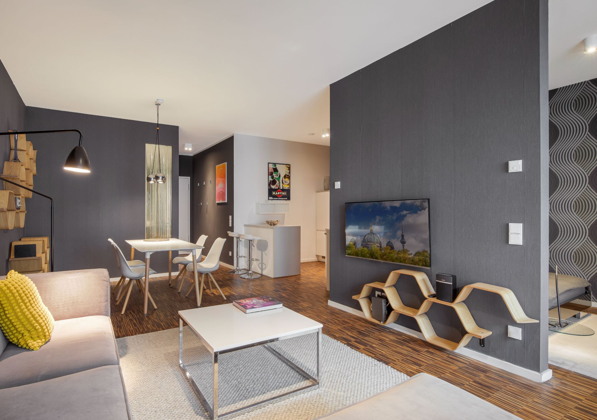Modernes Wohnzimmer mit grauer Wand, Sofa, Esstisch und Regal unter einem Fernseher.