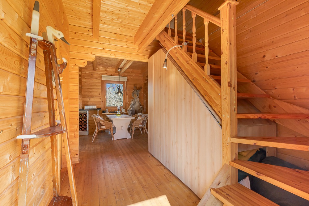 Holztreppe in einem hellen Raum mit Esstisch und Stühlen im Hintergrund.