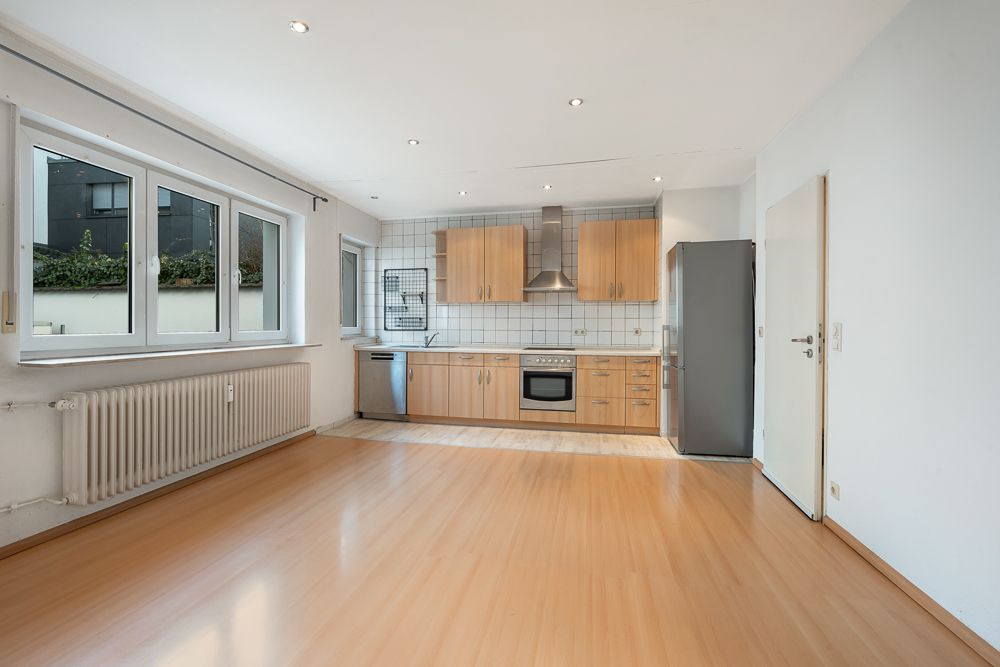 Helle Küche mit Holzboden, Einbauküche, drei Fenstern und Kühlschrank.